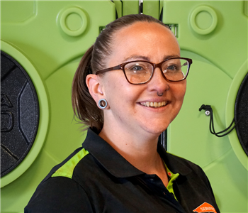 Smiling woman in SERVPRO uniform standing in front of green equipment