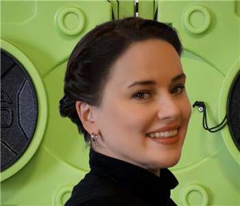 Smiling woman, in black dress in front of green machines